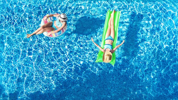 Young girls in swimming pool aerial drone view from above happy kids swim on inflatable ring donut