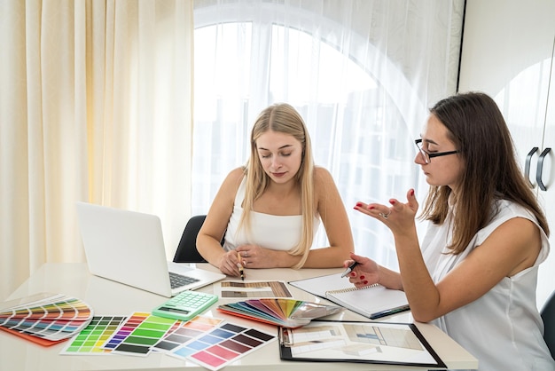 Young girls at the table sit and choose from among the color samples needed for home design