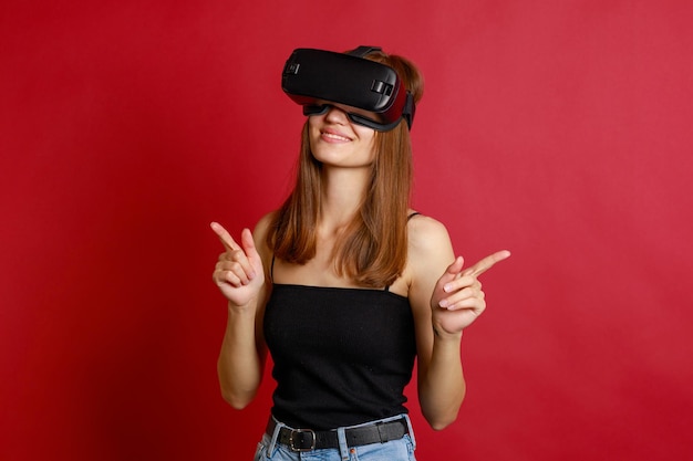 Молодые девушки в очках виртуальной реальности и указывая пальцами в сторону на красном фоне