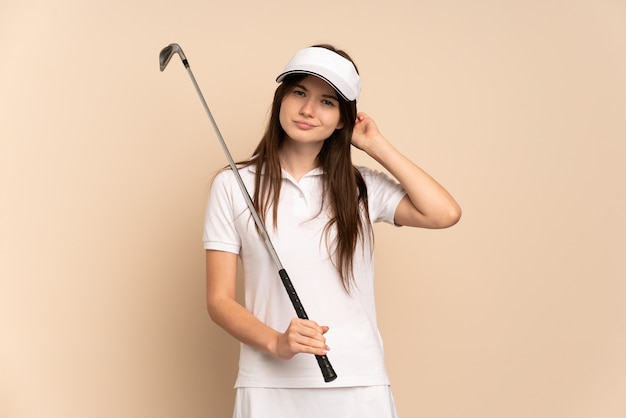 Young golfer girl isolated on beige having doubts
