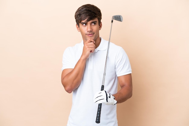 Young golfer player man isolated on ocher background having doubts and thinking