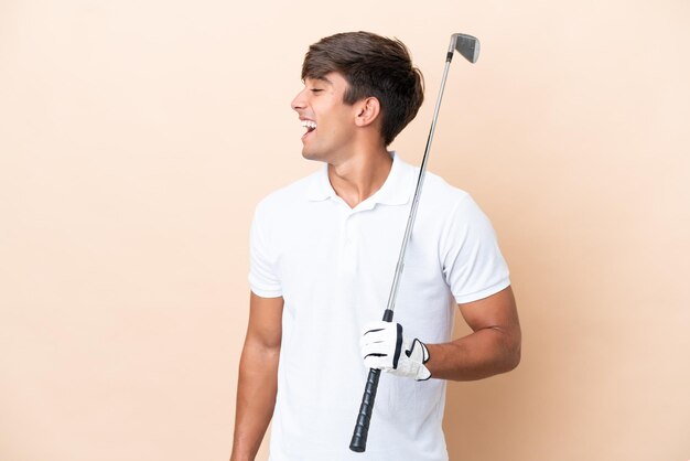 Young golfer player man isolated on ocher background laughing in lateral position