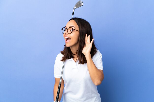 Young golfer woman over colorful wall listening to something by putting hand on the ear