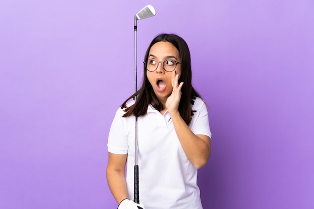 Young golfer woman over colorful wall whispering something with surprise gesture while looking to the side
