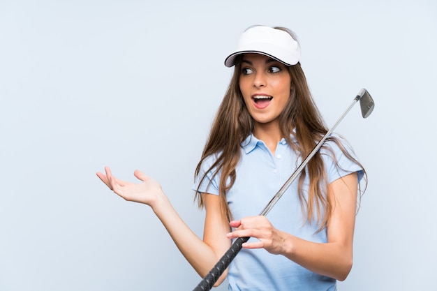 Молодая женщина гольфист над изолированной синей стеной с выражением лица сюрприз