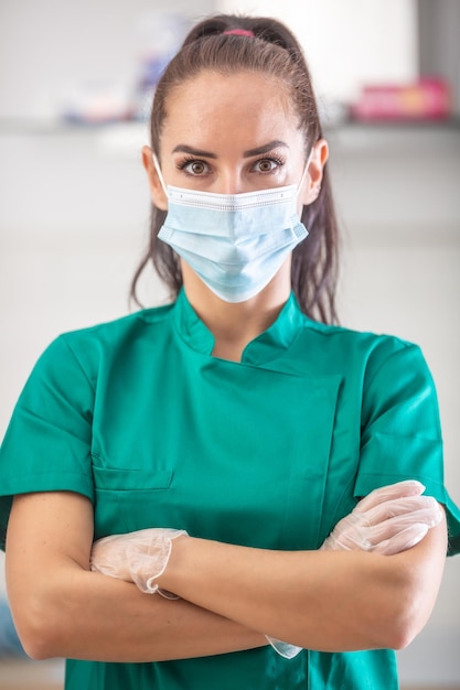 Young good-looking female healthcare worker in green wears face mask and protective gloves. standing with arms crossed.