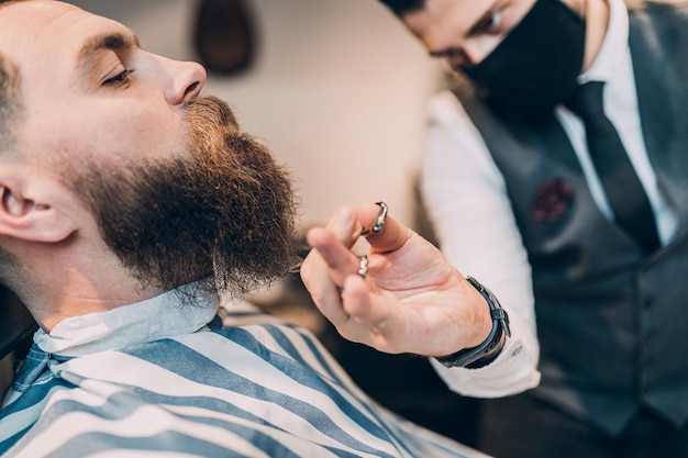 Young good looking hipste man visiting barber shop. Trendy and stylish beard styling and cut.