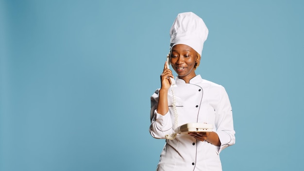 Photo young gourmet chef using retro landline phone to call people, having remote conversation in studio. professional cook with apron answering vintage office telephone with cord, phone line.