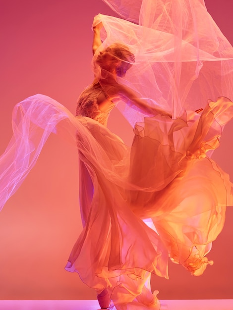 Young graceful female ballet dancer or classic ballerina dancing at red studio. Caucasian model on pointe shoes