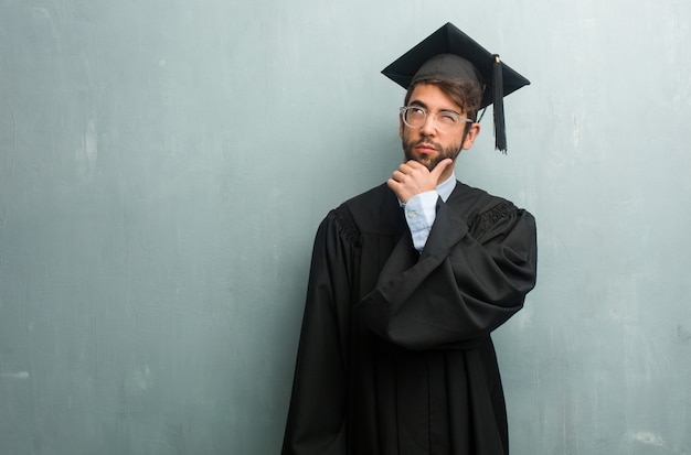 Young graduated man against a grunge wall with a copy space doubting and confused