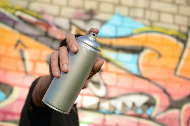 Young graffiti artist aims his spray can on background of colorful graffiti in pink tones