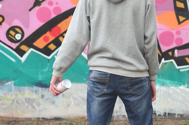 A young graffiti artist in a gray hoodie looks at the wall 