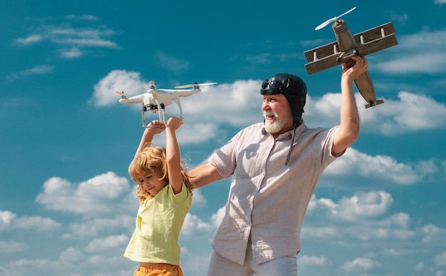 Young grandson and old grandfather with plane and quadcopter drone over blue sky and clouds backgrou