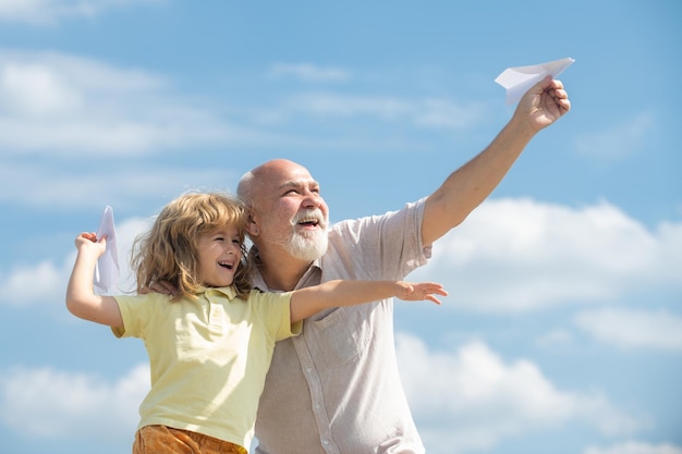 Young grandson and old grandfather with toy paper plane against summer sky background child boy with