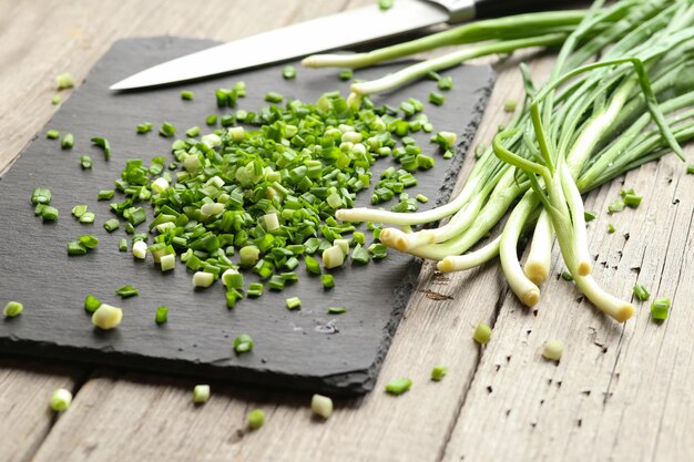 Photo young green onions cut into pieces on a black board on a wooden table cooking food healthy eating nongmo products fortified food