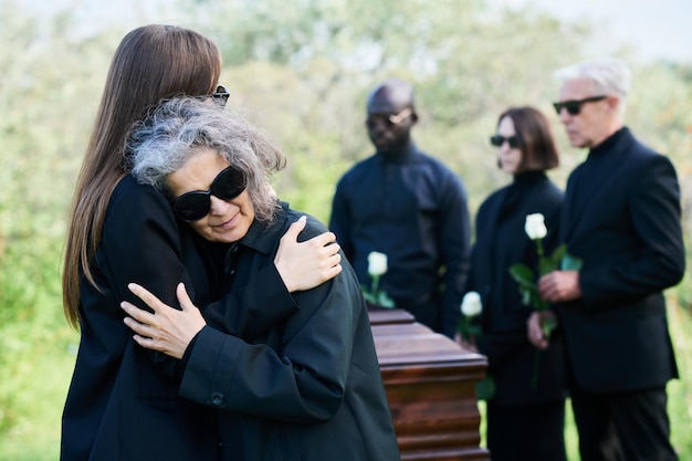 Photo young grieving woman giving hug to her mourning mother in sunglasses