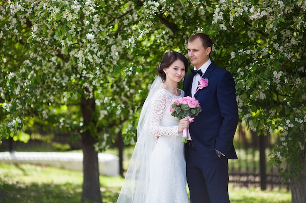 Young groom and bride with wedding bouquet in blooming garden