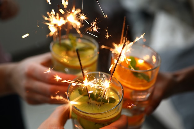 Young group friends hold in hand cocktail with sparkler