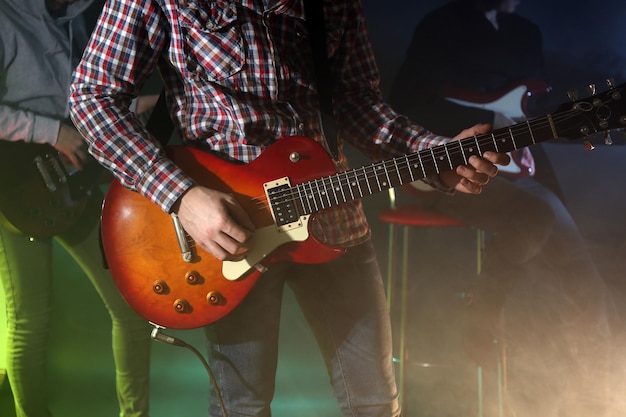 Young group playing electric guitar on lighted foggy background