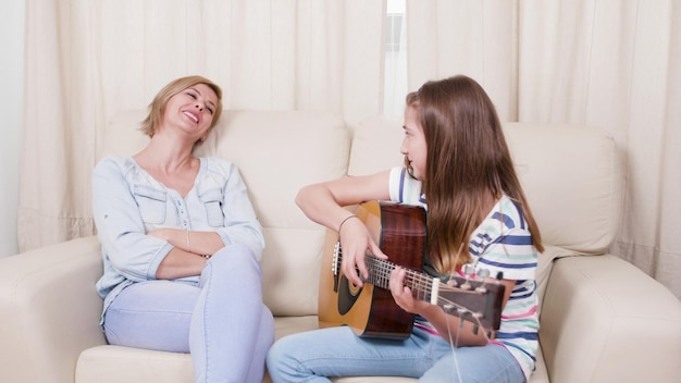 Giovane chitarrista bambino seduto sul divano accanto alla madre che tiene la chitarra che mostra come cantare per la lezione della scuola musicale godendosi lo strumento. bambino creativo che studia lezioni di musica. concetto di attività divertente