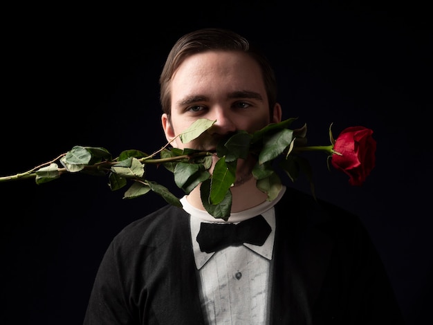 Young guy in a black t-shirt suit holding a red rose in his teeth on black