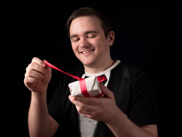 Young guy in a black t-shirt suit opens a white gift with a smile