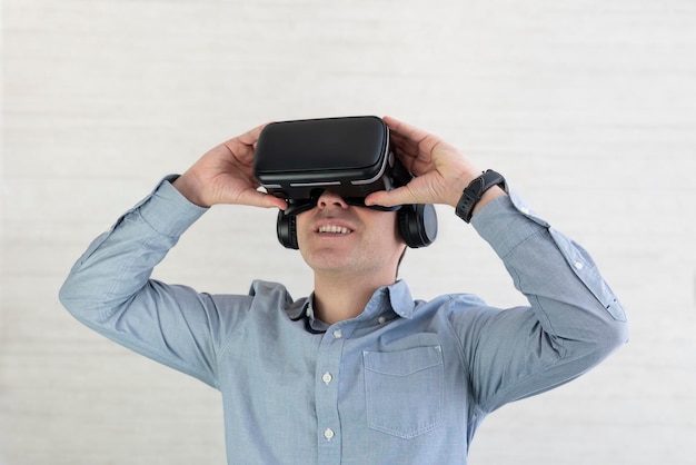 Молодой парень в повседневной одежде, использующий очки VR, прикасается к чему-то невидимому в копировальном пространстве. Тысячелетний человек, переживающий приключения в виртуальной реальности на сером студийном фоне. Панорама дополненной реальности