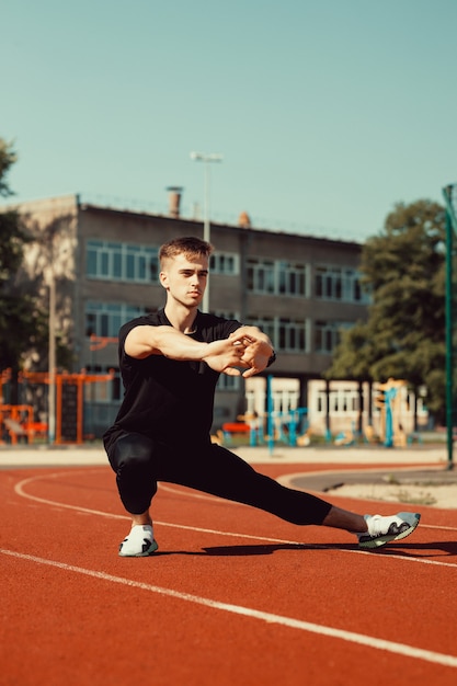 Young guy doing warm-up before sports exercise at school stadium