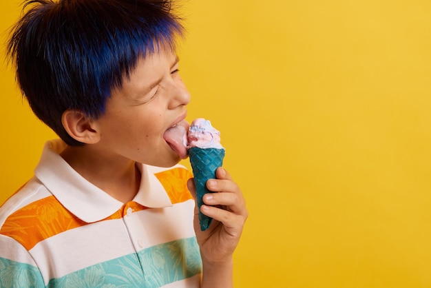 Foto giovane ragazzo che mangia un gelato appetitoso su un bastone su uno sfondo giallo