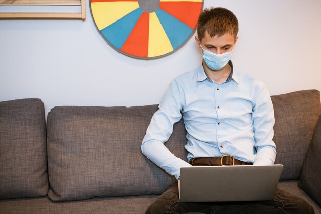 Foto un giovane ragazzo di aspetto europeo con una camicia leggera si siede in una maschera medica protettiva e lavora su...