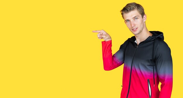 Young guy of European appearance on a yellow background. point your finger at an empty spot. Copy space