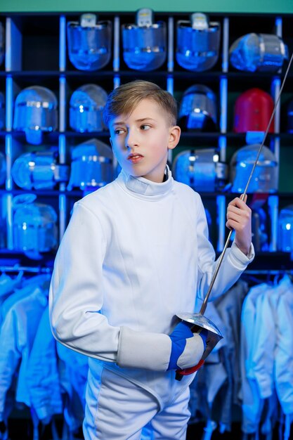 Young guy in a fencing suit with a sword in his hand, on a blue background, neon light. The athlete trains. Sports, youth, healthy lifestyle.