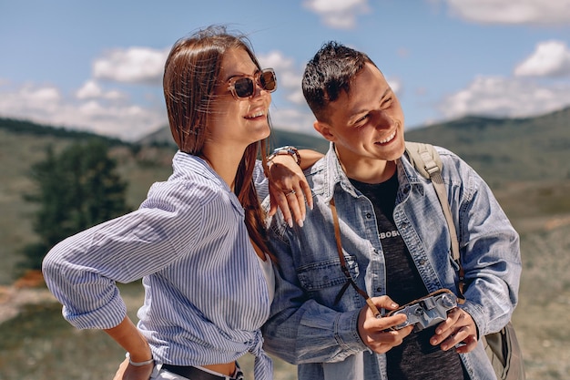 a young guy and a girl are standing on a blurry background with a green valley. holding the camera in your hands and looking away at the landscape.