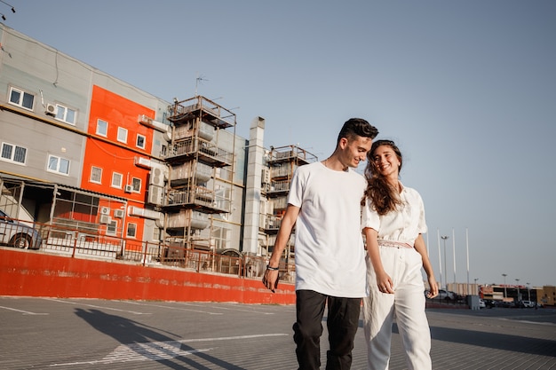 Young guy and girl are walking on the square on the background of urban building in the warm day .