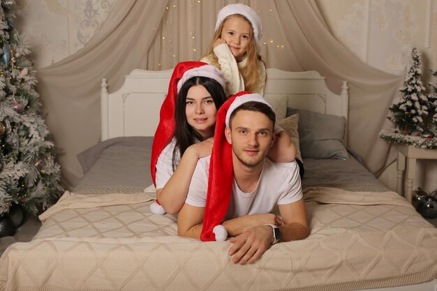 침대에 누워 산타 클로스 모자에 아기 소녀와 함께 젊은 남자 여자 가족 크리스마스