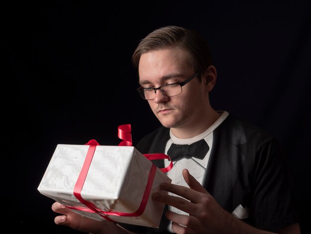 Young guy in glasses and black t-shirt suit looking at white gift on a black 