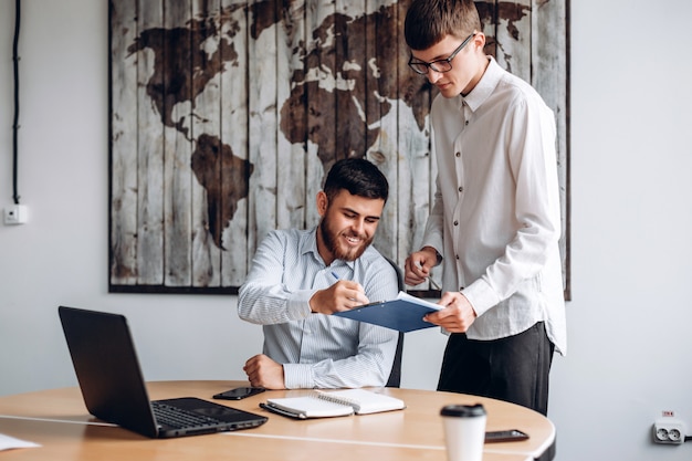 Young guy in glasses gives his boss documents to sign