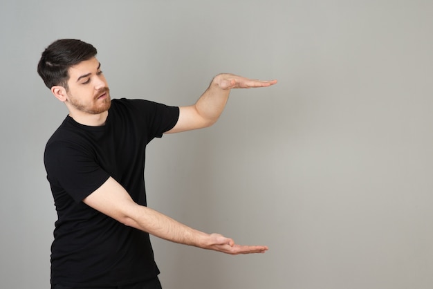 Young guy on a grey showing measurement with hands.