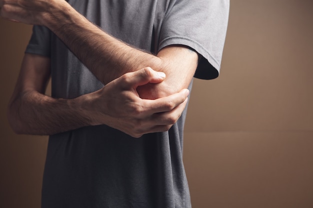 A young guy has a sore elbow on a brown background