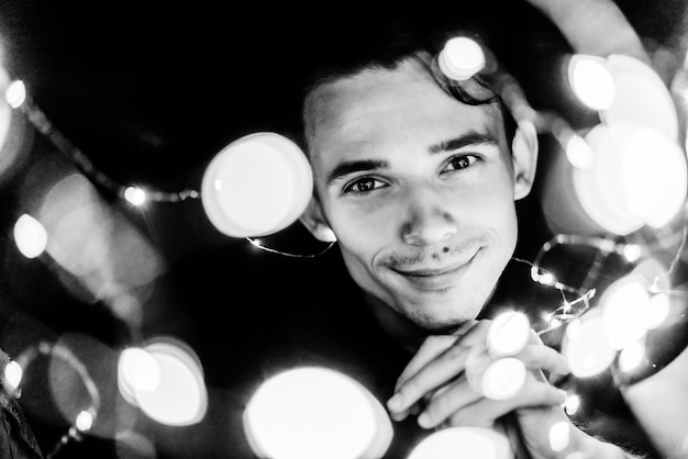 young guy holding glowing garlands at night black and white portrait selective focus