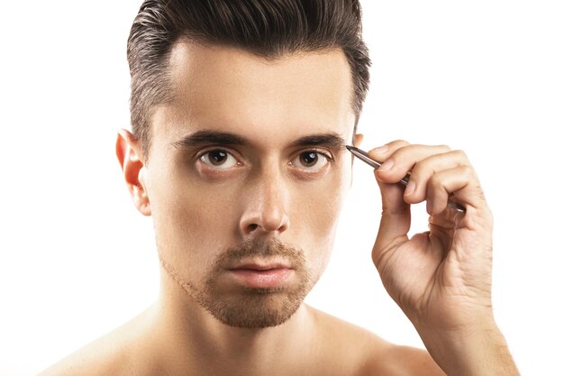Young guy holding tweezers near his eyebrow for thats shape correction