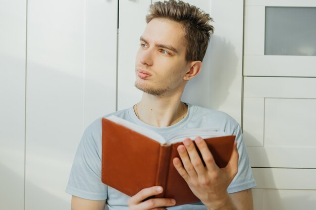 Фото Молодой парень в футболке дома читает книгу, останься дома