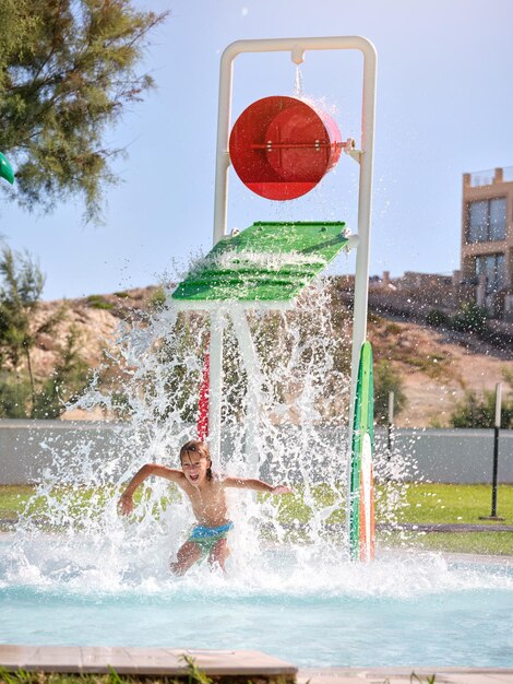 Young guy jumping with raised arms while falling water from bucket shower on sunny day