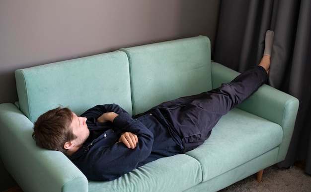 Молодой парень лежит и спит на диване дома днем