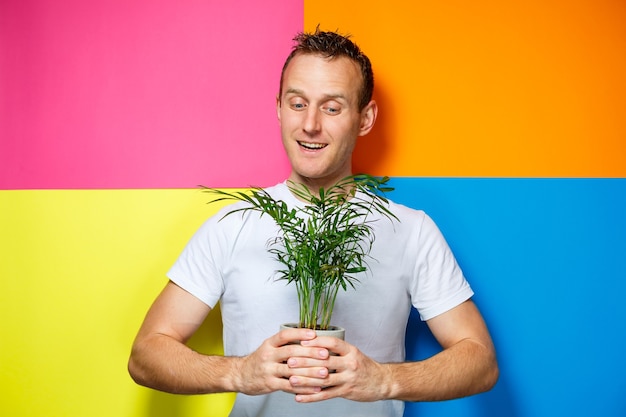 Young guy man in a white T-shirt, colorful background, decorative palm, emotions photo, home plant, love of nature