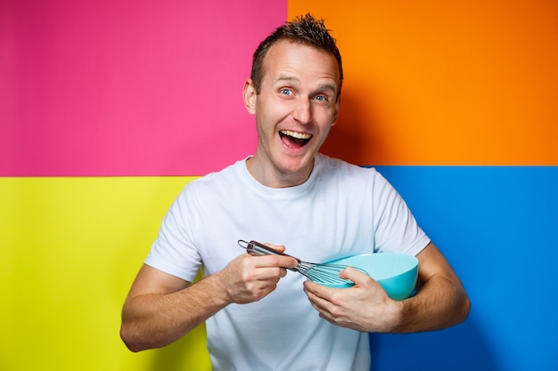 Young guy man in a white T-shirt, colorful background, kitchen utensils, cook, emotions photo