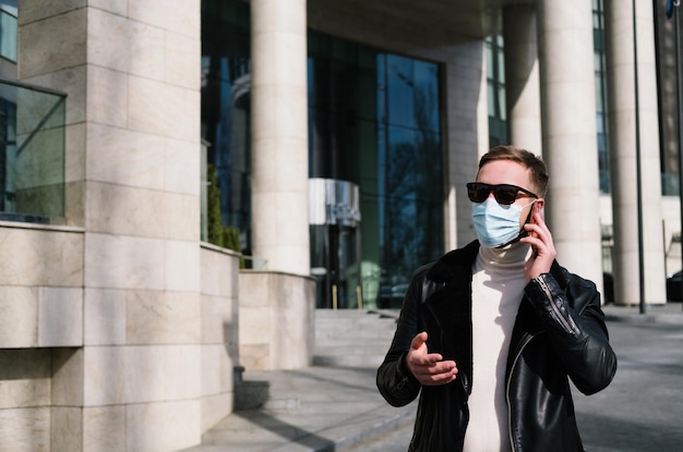 의료용 마스크를 쓴 젊은 남자는 거리에서 전화를 사용하고 검역 개념