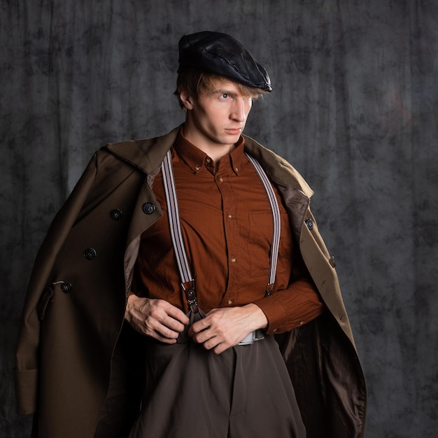 A young guy in militarystyle clothes a brown outfit and a flat cap on his head posing in the studio