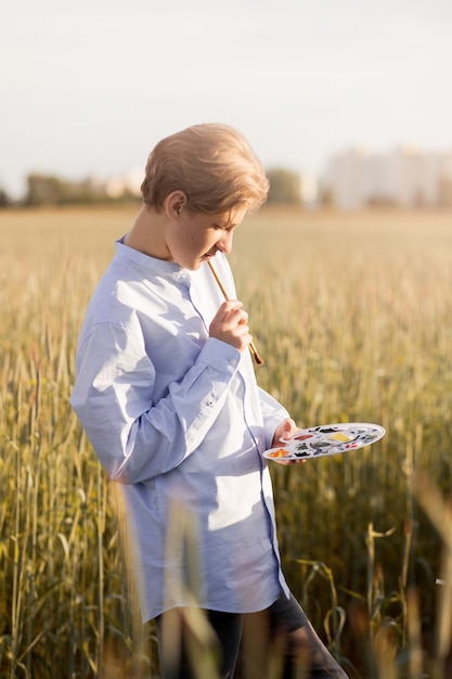 若い男は夏の自然の中でキャンバスにペイントします。自然界の芸術作品。 Plein Air。垂直