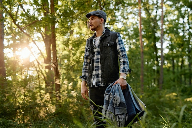 A young guy in a plaid shirt with a plaid walks in a sunny park in the forest